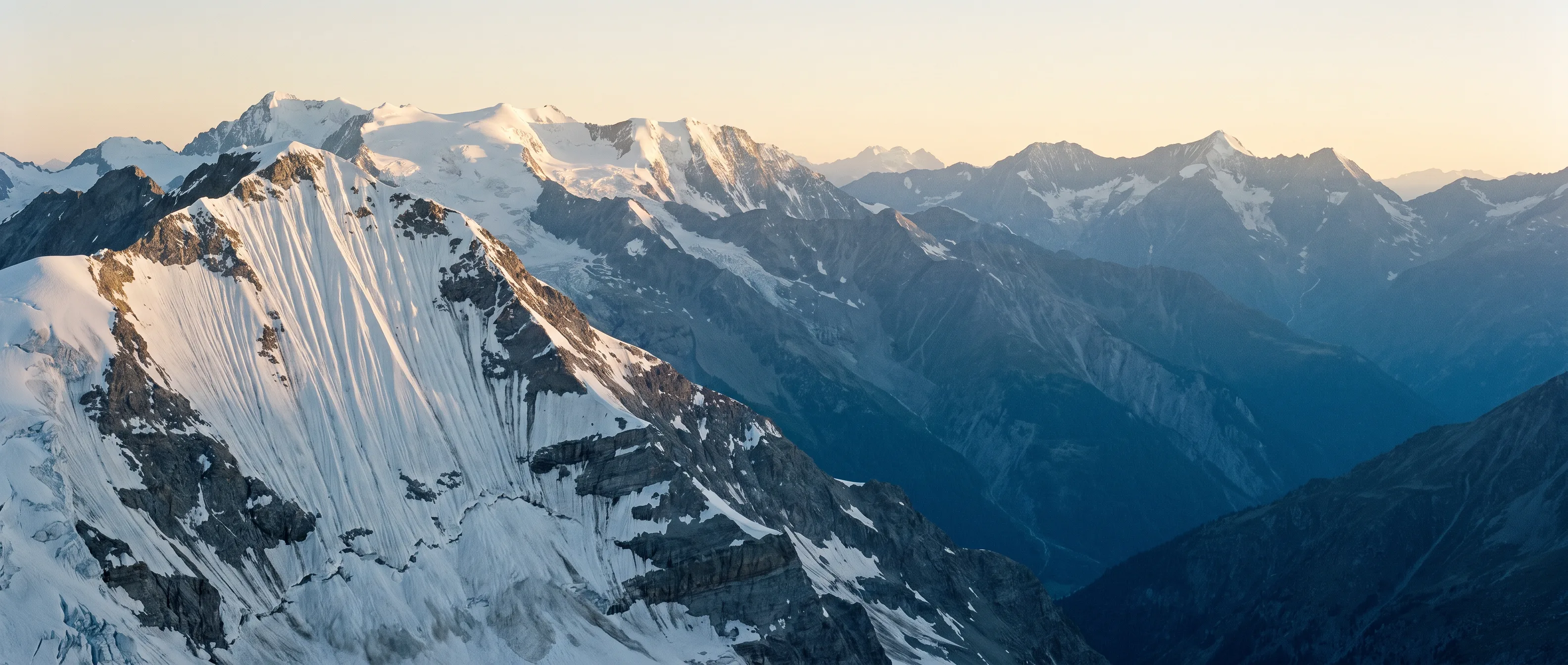 A glaciated alpine massif at dusk, ridgelines receding into blue shadow.